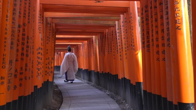 A Shinto priest walking through the famous torii gates at Fushimi Inari Shrine in Kyoto, Japan, slow motion shot.