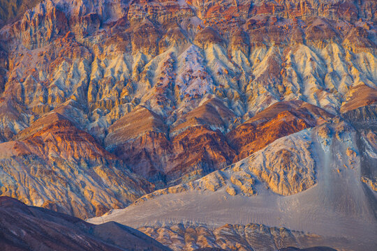 View of the colorful, layered rock formations of Death Valley National Park, featuring vibrant mineral deposits and rugged desert terrain illuminated by golden hour light in the United States.