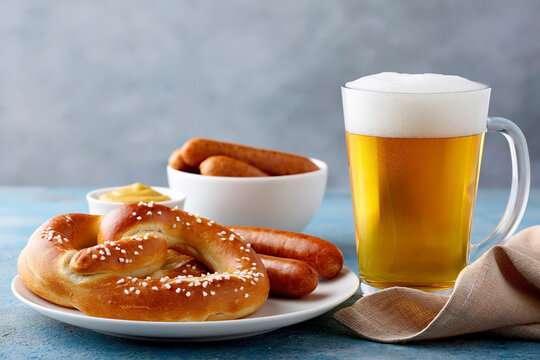 Traditional oktoberfest food with golden beer, salted pretzel, grilled sausages and mustard served on a table