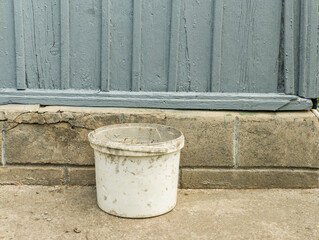 Naklejka premium White Plastic Bucket Sitting Near Foundation Wall Of Wooden House