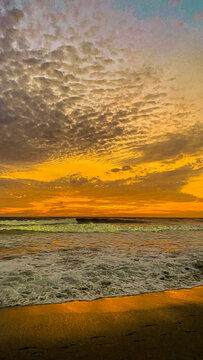 Abstract artistic view of golden yellow sunset sky with textured clouds reflecting on ocean waves and sandy beach