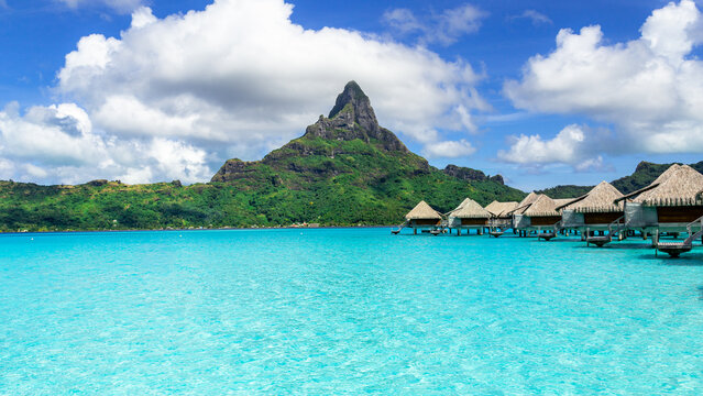 View of the iconic Mount Otemanu rising above turquoise lagoon waters and traditional overwater bungalows in Bora-Bora, Leeward Islands, French Polynesia.