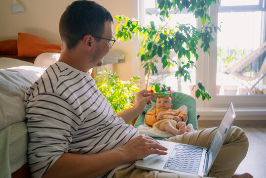 Father working on a laptop is distracted by playing with baby, showing the challenges and joys of balancing professional duties with family life in a home environment