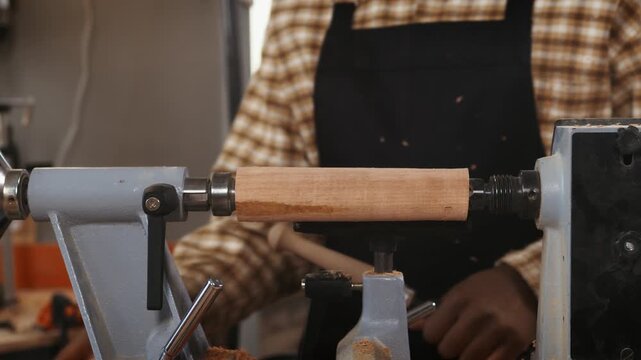 Craftsman turning wooden cylinder on lathe, shaping timber into round form during woodturning process in woodworking workshop with precision tools