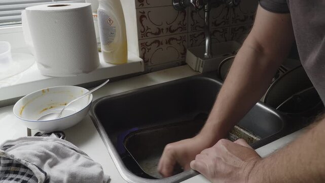 Liquid detergent is used to tackle baked-on residue during a thorough kitchen cleanup. A relatable domestic scene highlighting cleanliness, home care, and everyday household tasks.