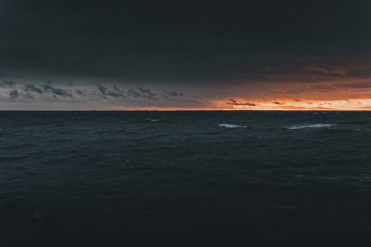 View of the dramatic sunset over the dark waters of the Baltic Sea at Saxby rannik, featuring a vibrant orange horizon and deep blue storm clouds Saxby, Laane maakond, Estonia.