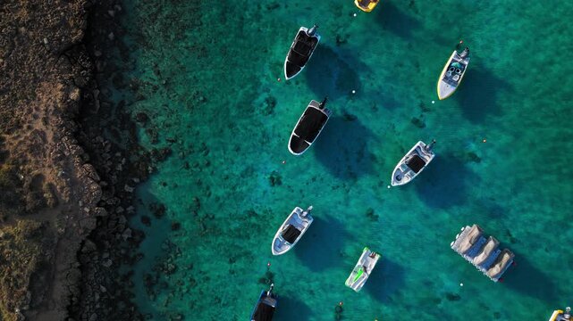 Top-down drone view of Fig Tree Beach in Protaras, Cyprus. Boats and tourists gather in a sheltered turquoise cove surrounded by rocky formations.