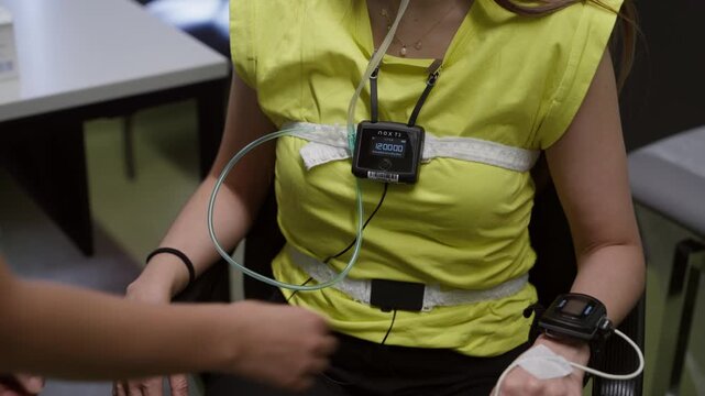 A healthcare worker prepares a woman for a sleep study by adjusting diagnostic monitoring equipment and sensors. Useful for medical technology and wellness content.
