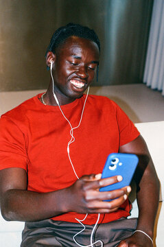 Man in red shirt using smartphone white earphones. film photo
