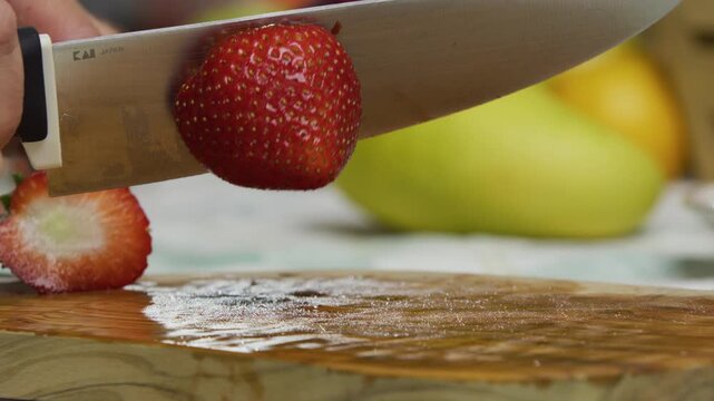 Closeup, slow motion shot of knife slicing through strawberry