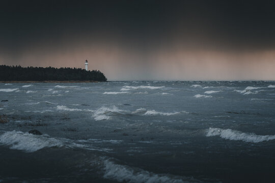 View of Saxby Lighthouse standing on the coast amidst a stormy sea with dark clouds and crashing waves in Saxby, Laane maakond, Estonia.