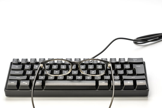 Clear frame eyeglasses placed on top of black wired mechanical keyboard on white background concept of myopia