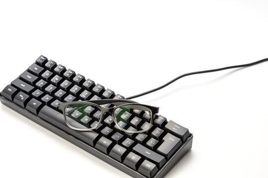 Modern black eyeglasses placed on top of compact black mechanical gaming keyboard on white background, nearsighted