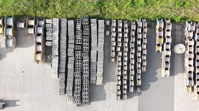Aerial view of a cable production plant warehouse showing organized rows of cable spools on a concrete surface with green grass and trees surrounding the area. Industrial place