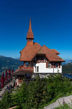 View of the Harder Kulm restaurant with its distinctive red-tiled roof and tower, set against a clear blue sky with mountain views in Unterseen, Canton of Bern, Switzerland.