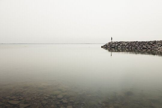 Saxby, Laane maakond, Estonia - 01 June 2025: View of a lone person standing on the rocky Saxby rannik coastline overlooking the calm, misty Baltic Sea under a pale sky.