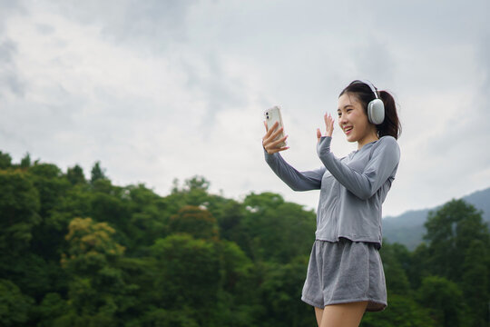 Smiling woman with wireless headphones taking selfie outdoors in activewear, illustrating connected lifestyle, mobile photo capture, and self-expression through digital platforms.