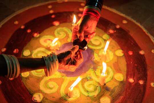 View of hands lighting traditional clay lamps on a vibrant rangoli pattern during Diwali celebrations in Rahim Yar Khan, Punjab, Pakistan.
