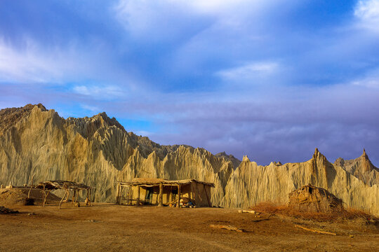 View of traditional mud huts set against the dramatic, eroded rock formations of Hingol National Park under a cloudy sky in Awaran, Balochistan, Pakistan.