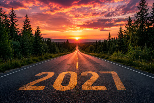 A scenic road leading into the horizon with the year 2027 painted on the asphalt at sunset time.