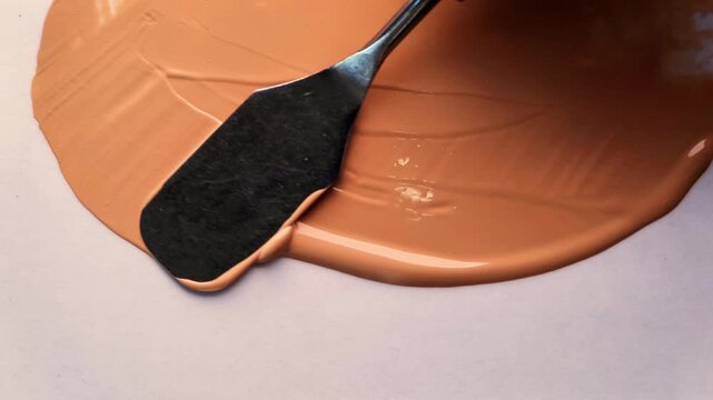 Smooth Liquid Foundation Texture Smudge by Palette Knife on Neutral Background. High-angle close-up shot demonstrating the ultra-smooth texture of a premium liquid foundation fluid.