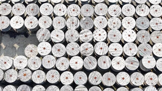 Aerial view of a warehouse displaying a large arrangement of wooden cable reels organized in rows, showcasing a systematic layout across the expansive concrete surface. Industrial place