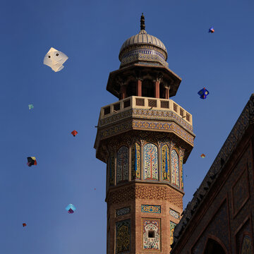 View of the ornate minaret of Wazir Khan Mosque with intricate tile work against a clear blue sky filled with colorful kites during the Basant festival, Lahore, Punjab, Pakistan.