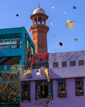 View of the historic minaret rising above colorful buildings adorned with festive decorations during the Basant kite festival in Lahore, Punjab, Pakistan.