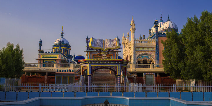 View of the ornate Jamia Masjid Bhong Sharif with its intricate tile work, domes, and a central structure resembling an open book in Bhong, Punjab, Pakistan.