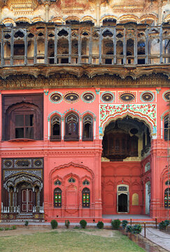 View of the ornate red facade of the historic Umar Hayat Mahal Library featuring intricate wooden balconies, carved arches, and decorative patterns in Chiniot, Punjab, Pakistan.