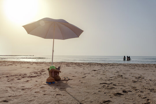 Beach umbrella with backpack hat sunglasses and flip flops by the sea