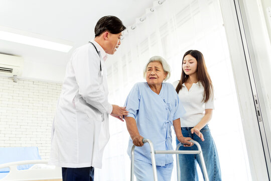 Doctor and caregiver assist an elderly patient using a walker during a hospital consultation in a bright recovery room