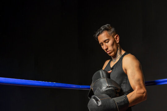 Focused Hispanic boxer preparing for training in boxing ring with dark background