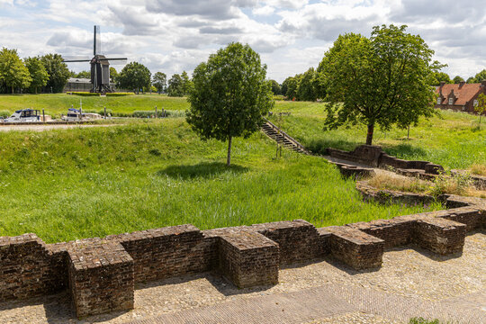 View of the historic brick fortification walls and a traditional windmill in the background, surrounded by lush green grass and trees in Heusden, North Brabant, Netherlands.