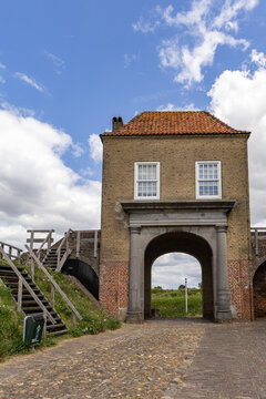 View of the historic Wijkse Poort city gate with brick masonry, an arched stone entrance, and wooden stairs leading to the ramparts in Heusden, North Brabant, Netherlands.