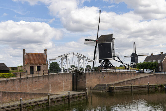 View of a traditional Dutch windmill and a white drawbridge over a canal with historic brick fortifications in Heusden, North Brabant, Netherlands.