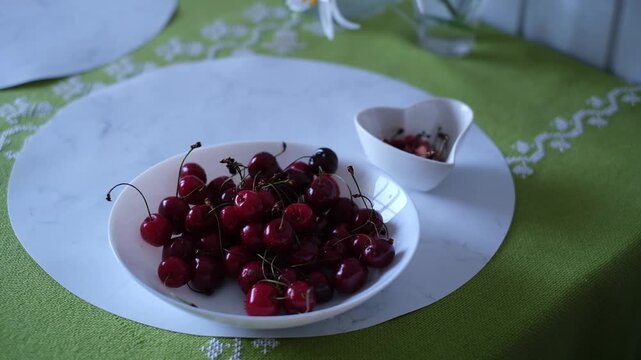 Picking cherries from a bowl in a kitchen on a green tablecloth during the afternoon