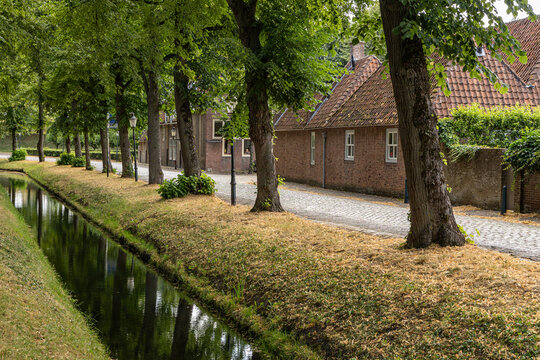 View of a quiet cobblestone street lined with mature trees and a narrow canal in the historic town of Heusden, North Brabant, Netherlands.