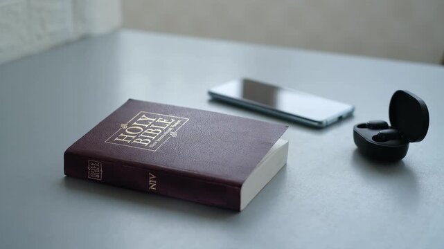 Reading the Holy Bible with a smartphone and earbuds on a table
