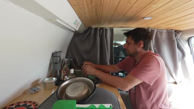 Young man washing dishes inside camper van kitchen embracing van life and nomadic style