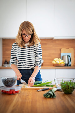 Mid-aged woman chopping fresh vegetables on a wooden cutting board in a modern kitchen