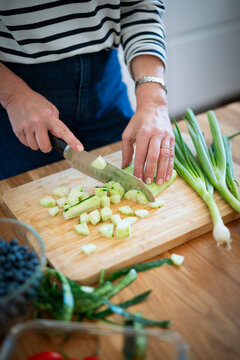 Mid-aged woman chopping fresh vegetables on a wooden cutting board in a modern kitchen