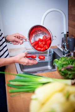 Hands washing fresh cherry tomatoes in a colander under running water