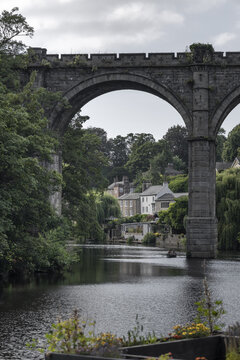 View of the historic Knaresborough Viaduct spanning the River Nidd with lush trees and stone buildings in the background in Knaresborough, England, United Kingdom.