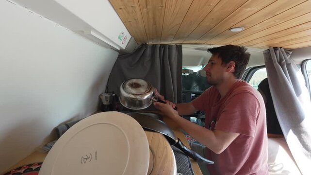 Young man washing dishes inside camper van kitchen embracing van life and nomadic style