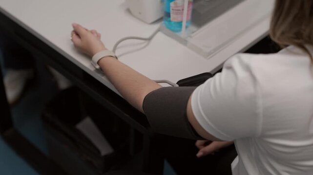 High angle close up of a woman having her blood pressure measured using a digital cuff in a medical office or clinic setting. Useful for healthcare and wellness content.