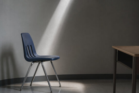 detention. Empty school chair with beam of cold daylight beside plain wall, discipline and silent reflection concept, lifestyle magazines.