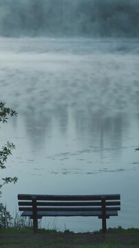 Empty wooden bench facing still lake in morning haze