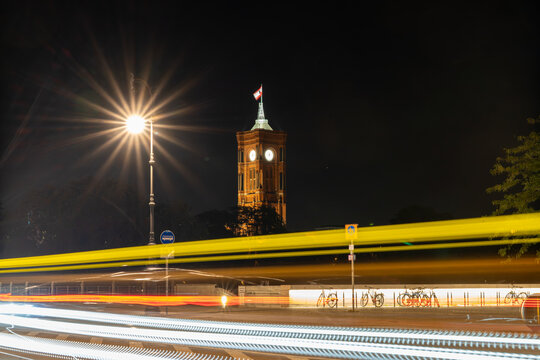 View of the illuminated Rotes Rathaus at night with vibrant light trails from passing traffic and a glowing street lamp in Berlin, Berlin, Germany.