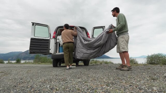 Couple preparing a bed inside their camper van with lake and mountains in the background